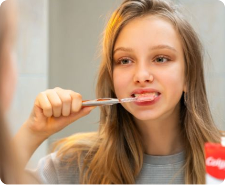 Menina escovando os dentes em frente a um espelho como parte de uma rotina saudável de higiene bucal.