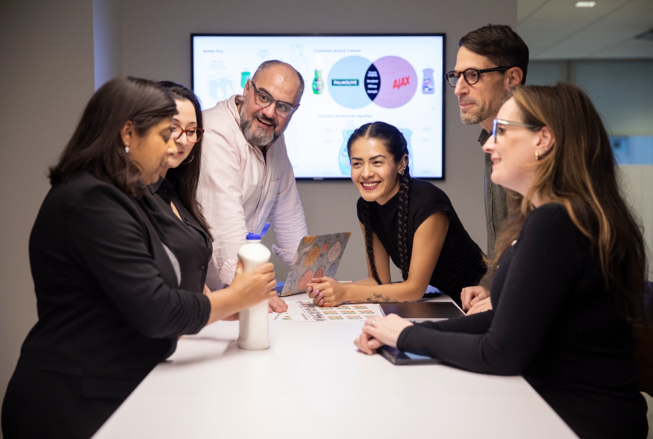 Seis funcionários da Colgate-Palmolive numa sala de reuniões a discutir um conceito de produto, com um diapositivo de apresentação num ecrã atrás deles.